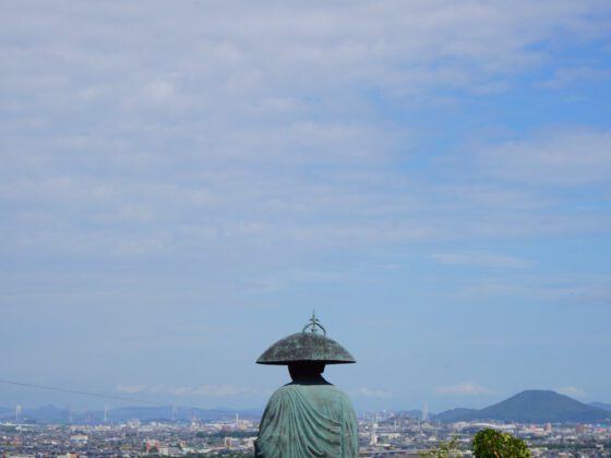 A statue of a monk overlooking an urban landscape under a blue sky: Shikoku Henro trail