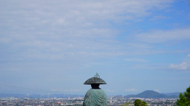 A statue of a monk overlooking an urban landscape under a blue sky: Shikoku Henro trail